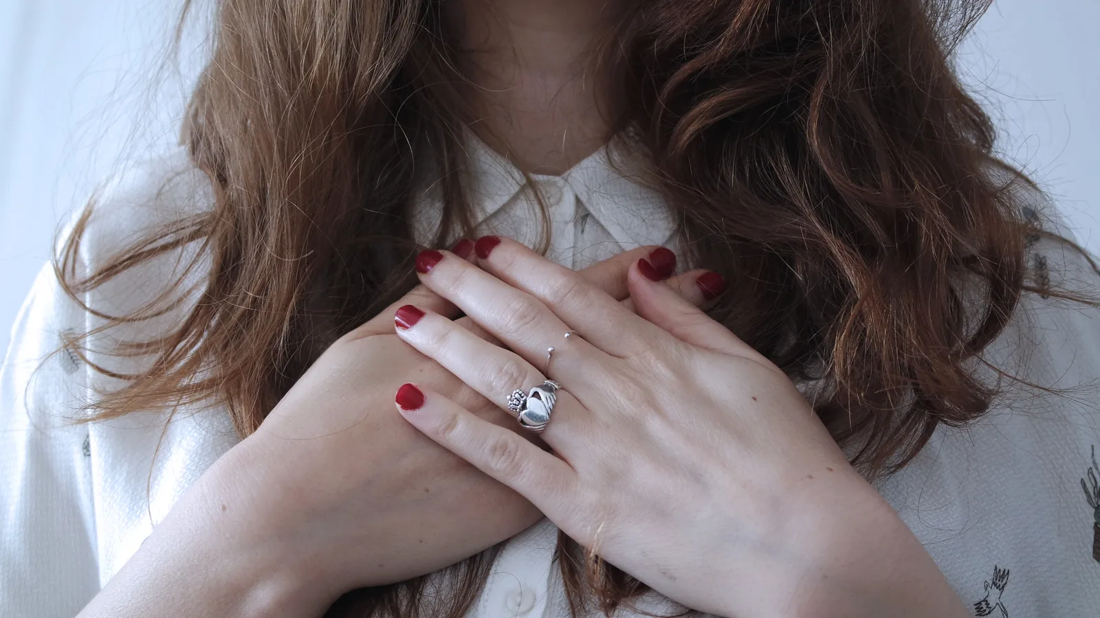 Hands with red polished nails crossed over a white shirt